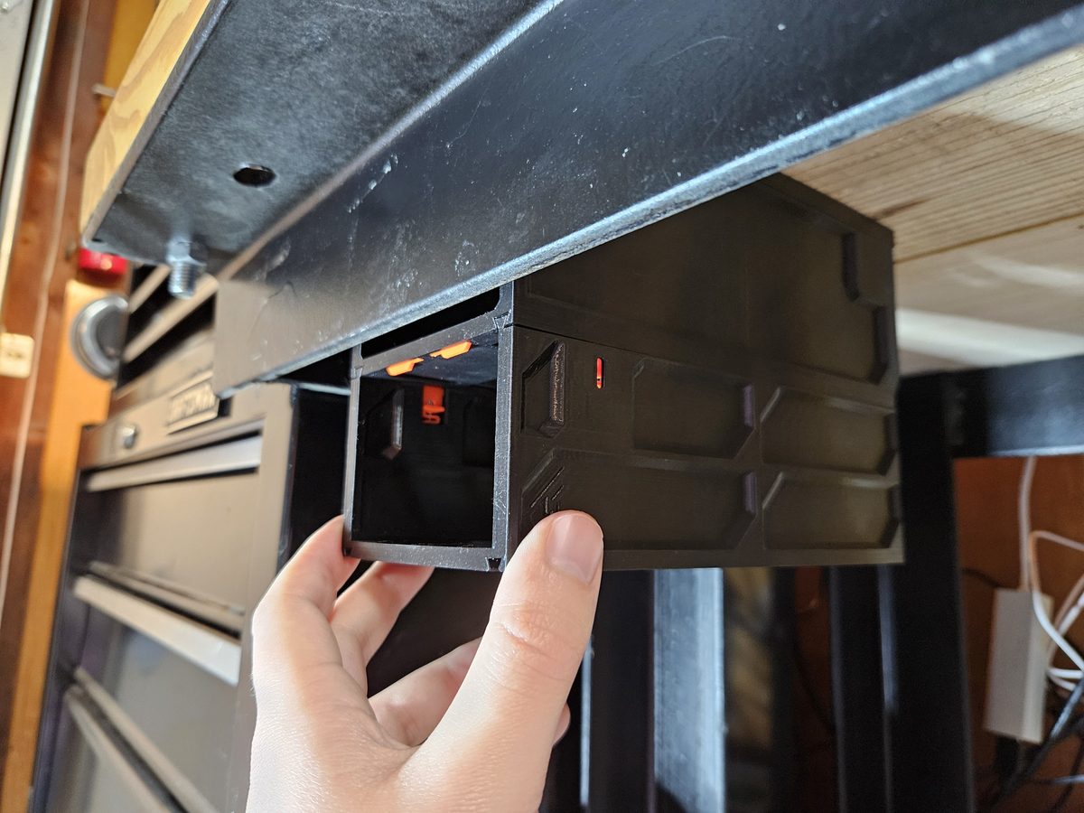 A hand lifting a small black case, orange QuickLocks in its walls, up to a case already hanging under a bench