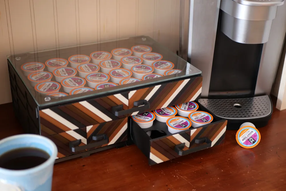 A coffee station: a MODULITH build with a glass top holding coffee pods, a drawer open below it, beside a brewer and a mug.