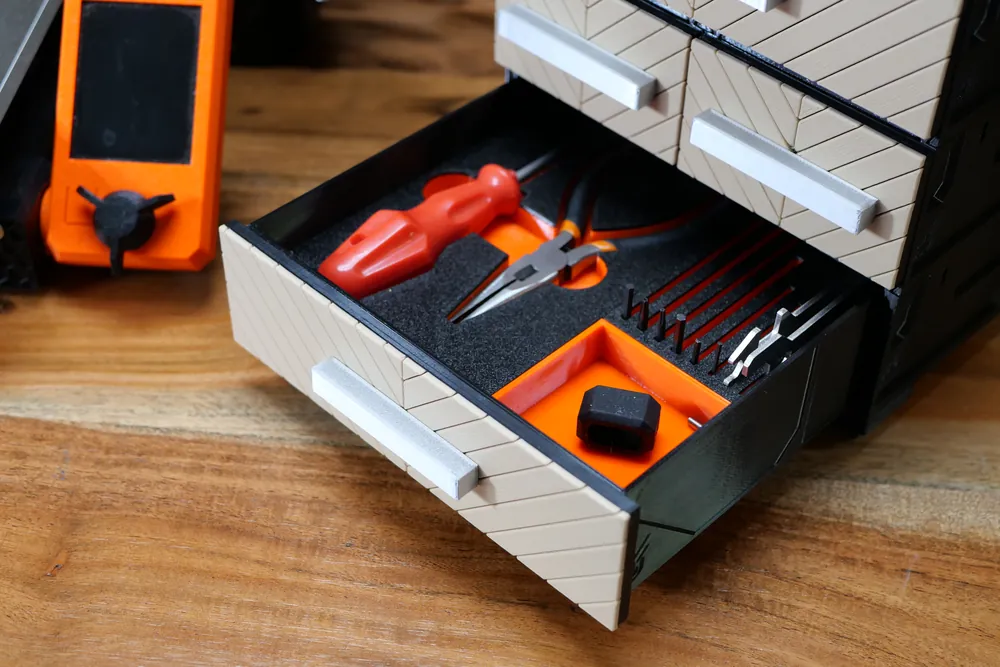 An open drawer with a 3D-printed tool insert holding a screwdriver, pliers and a row of hex keys, an orange compartment beside them.