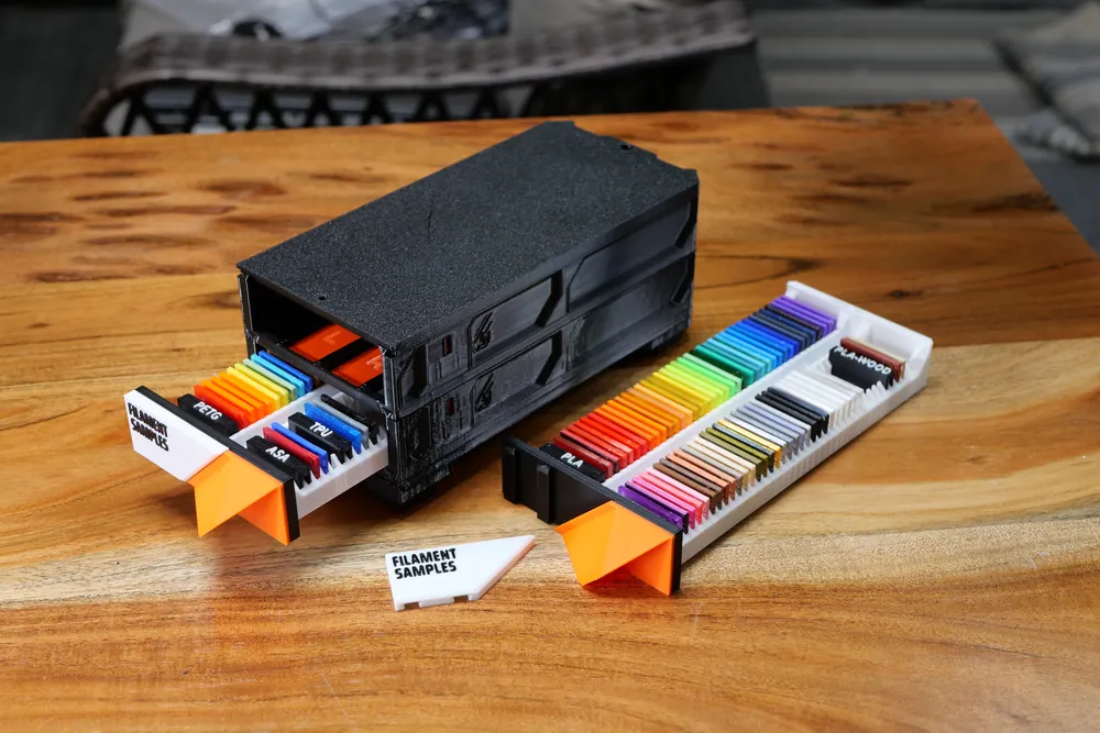 An open drawer with filament sample chips fanned out across a wooden desk.